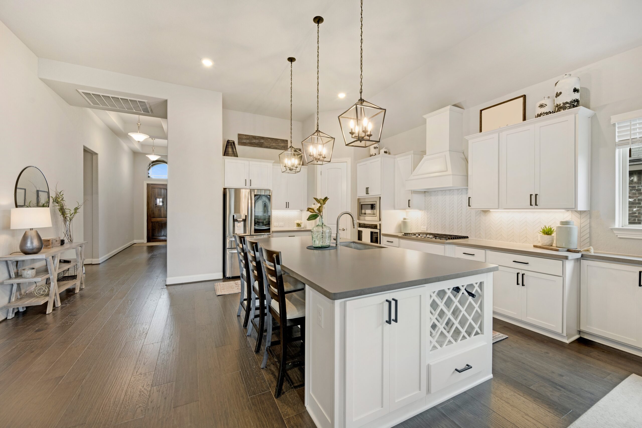 Modern kitchen with white cabinets, large island, pendant lights, and stainless steel appliances.